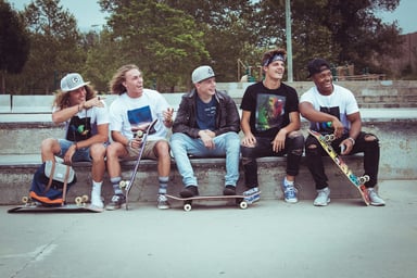 Five group of men sitting together with their skateboards.